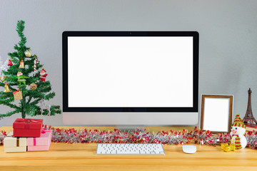 Merry Christmas and Happy New Year 2018! Celebrating holiday in modern office,Computer display on table with isolated white screen for mockup in x-mas time. Christmas tree with gifts decorations - obrazy, fototapety, plakaty