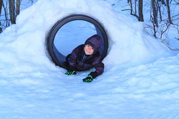 Happy boy playing in a snow tunnel. Real little boy has fun in the snow installations of public...