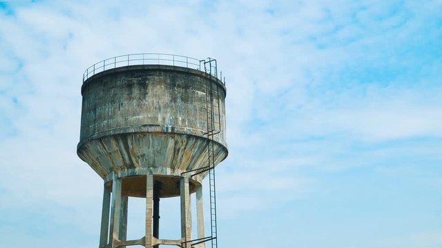 Old concrete water tower in front of blue sky - timelapse video.