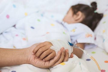 Mother hand holding sick daughter hand who have IV solution bandaged with love and care while she...