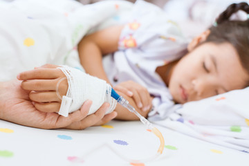 Mother hand holding sick daughter hand who have IV solution bandaged with love and care while she...