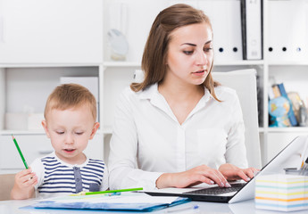 Woman is working on laptop while kid painting on papers