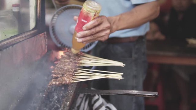 Man barbecuing satay over huge fire popular food in Malaysia, Indonesia and Thailand.