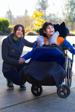 Disabled boy in wheelchair sitting with his caregiver outdoors