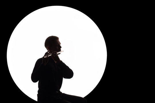 Silhouette of a guy in a white circle who plays the flute. Concept music for the full moon. Copy space. Night background.