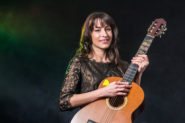 Fototapeta premium A beautiful girl with dark hair is holding a guitar on a smoky background. Green blue illumination.