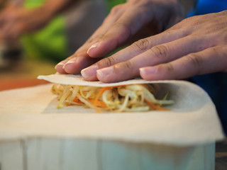 preparing thai spring rolls by hands on a wooden plate