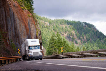 Big rig semi truck with reefer trailer transporting cargo on winding road with a rock on one side...