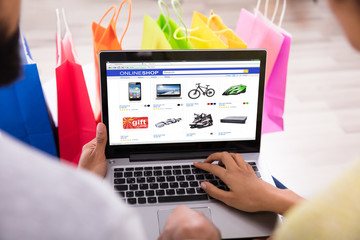 Couple Shopping Online In Front Of Multi Colored Shopping Bags