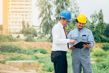 Asian engineer holding art boad work concept teamwork of building construction. Project contractor reviewing plan work in construction site.