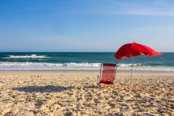 red chair and red umbrella on a sunny day at the beach - obrazy, fototapety, plakaty
