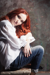 Fototapeta na wymiar Portrait of a beautiful girl with long red hair in a white man's shirt on a dark background in the studio