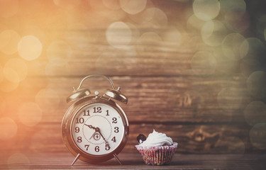 Metal alarm clock and cream cupcake