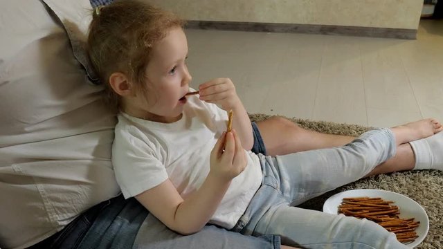 man and daughter watching television, sitting on the floor eating snacks