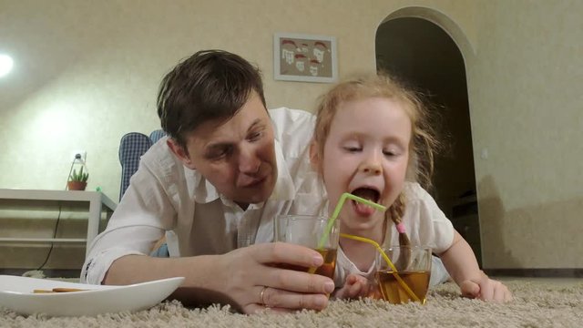 man and daughter watching television, sitting on the floor drink juice