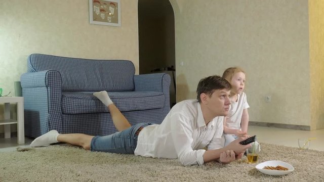 man and daughter watching television, sitting on the floor eating snacks