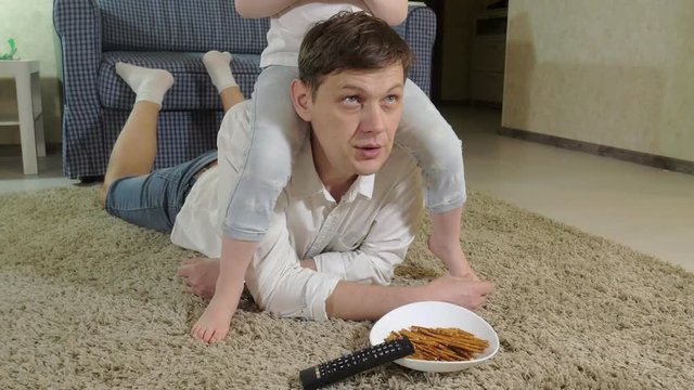 man and daughter watching television, sitting on the floor eating snacks