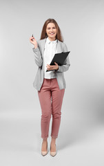 Fototapeta premium Beautiful young woman in elegant suit and with clipboard on light background