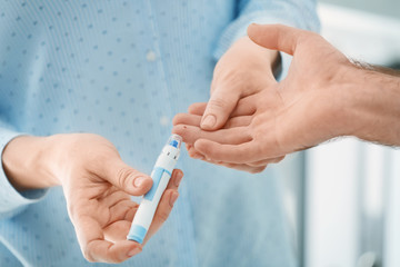 Doctor taking sample of diabetic patient's blood using lancet pen, closeup