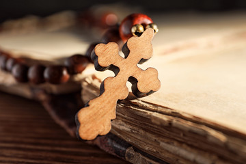 Rosary beads with wooden cross on old book, closeup