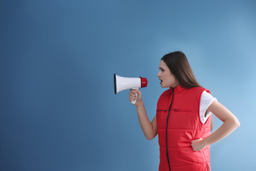 Young woman in red vest with megaphone on color background
