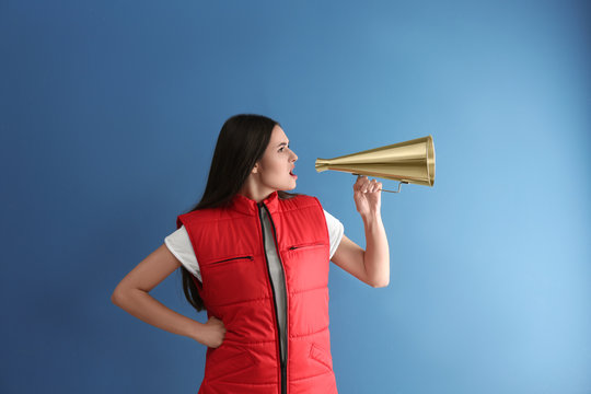 Young woman in red vest with megaphone on color background