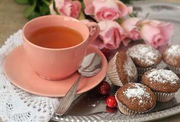 Tea in a porcelain pink cup, chocolate muffins, pink roses. Close-up