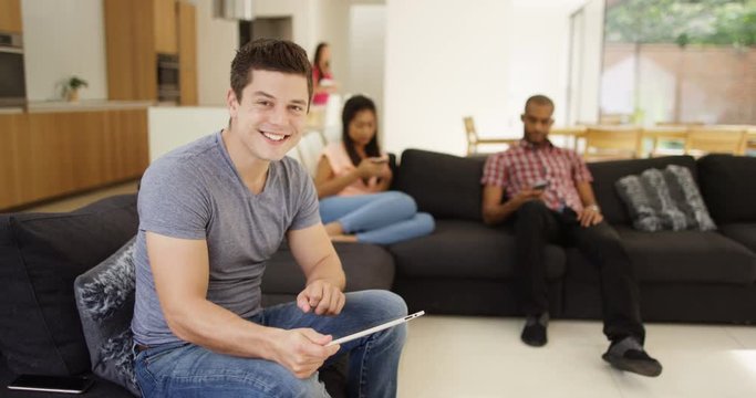 4K Happy group of friends relaxing at home with technology, attractive man turns to smile at camera. Slow motion