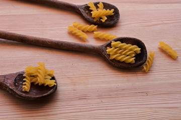 raw Italian spiral paste scattered on wooden spoon at wooden background/ space for text