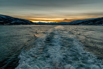 Sea view from moving ship to the sunset behind the mountains. Trace on the surface of water from propeller of a ship. Night time. Low key