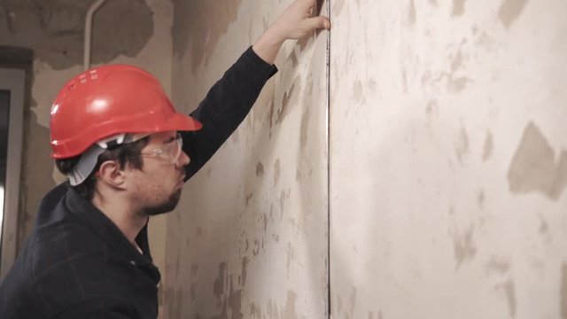 Portrait of adult men in a helmet on his head, the builder izmeret size walls with moposchyu centimeters worker wants to apply wallpaper in the apartment, which is being renovated