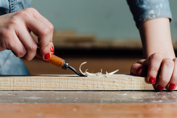 close-up carpenter woman's hand with a red manicure treats the tree, cuts the shavings.