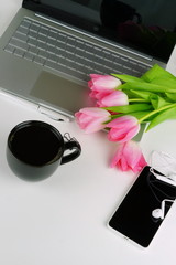 Flat lay, top view office feminine desk, workspace with laptop, cup of coffee, smartphone and bouquet pink tulips.Holidays concept.Copy space