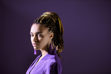 Naklejka na ściany i meble Fashionable african american girl posing in trendy purple jacket, isolated on dark purple
