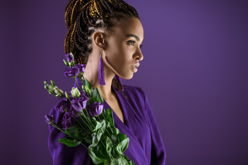 Fashionable african american girl posing with purple eustoma flowers, isolated on purple, ultra...