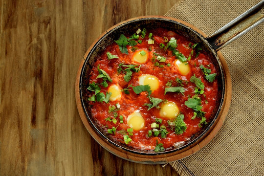 Fried eggs with tomato sauce and parsley in a cast iron pan. Shakshuka a traditional meal of the Jewish cuisine
