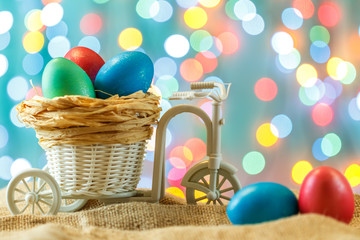 Easter card, colored eggs in the nest. Toy Bicycle with a cart. happy Easter. Delicate blue background. Place for text.