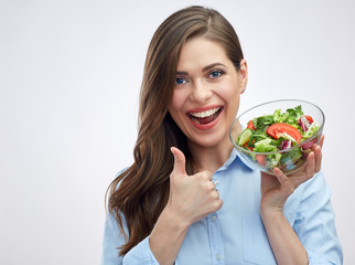 Happy young woman holding glass bowl with salad and showing thum