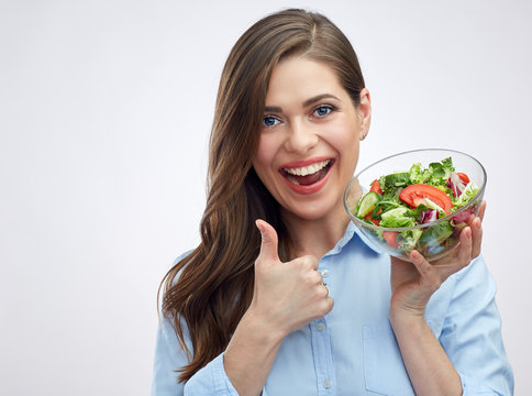 Happy young woman holding glass bowl with salad and showing thum