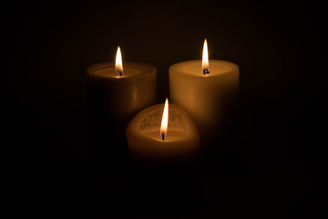 Set of three burning candles against a dark background
