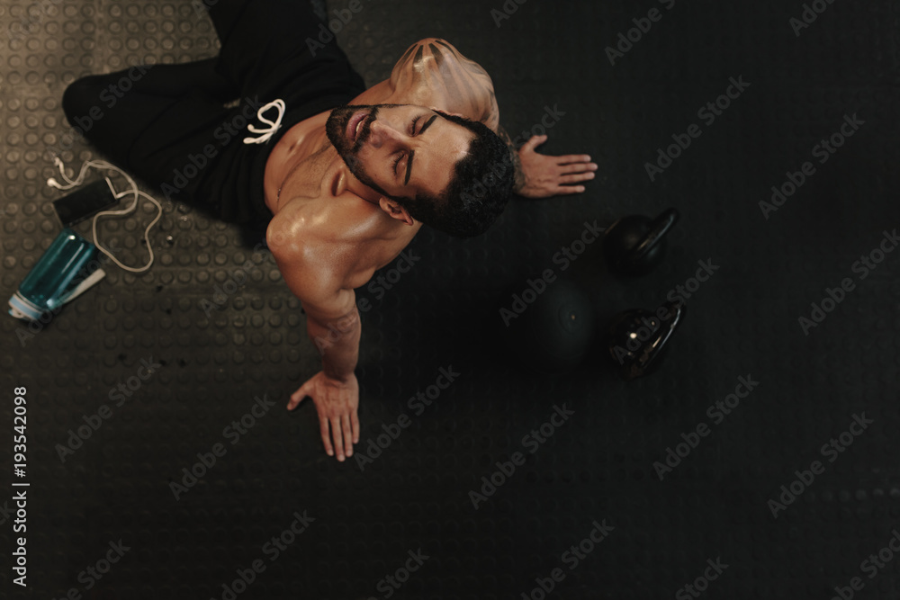 Wall mural Exhausted man relaxing on gym floor after workout