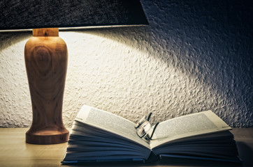 The opened book with spectacles under the lamplight