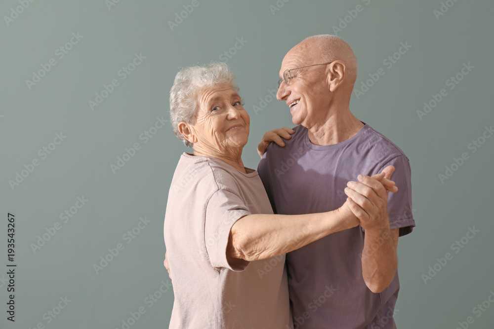 Wall mural Cute elderly couple dancing against color background