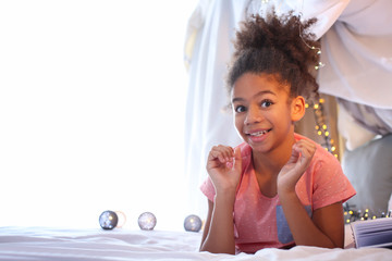 Cute African American girl lying on bed