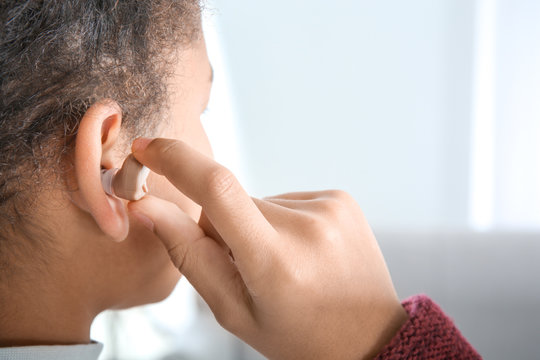 Little girl putting hearing aid in ear, closeup