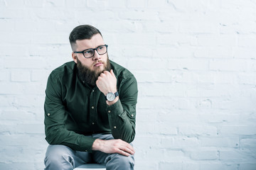 portrait of pensive businessman sitting on chair against white brick wall