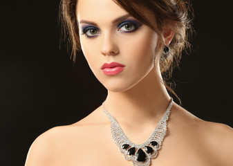 Beautiful young woman with elegant jewelry on dark background