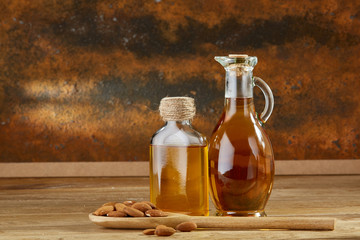 Aromatic oil in a glass jar and bottle with almond in a scoop on wooden table, close-up.