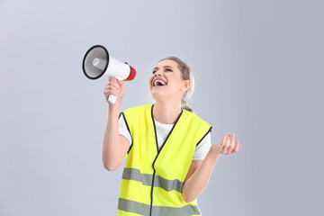 Young woman in reflective vest with megaphone on grey background