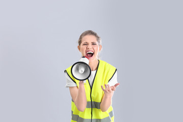 Fototapeta premium Young woman in reflective vest shouting into megaphone on grey background